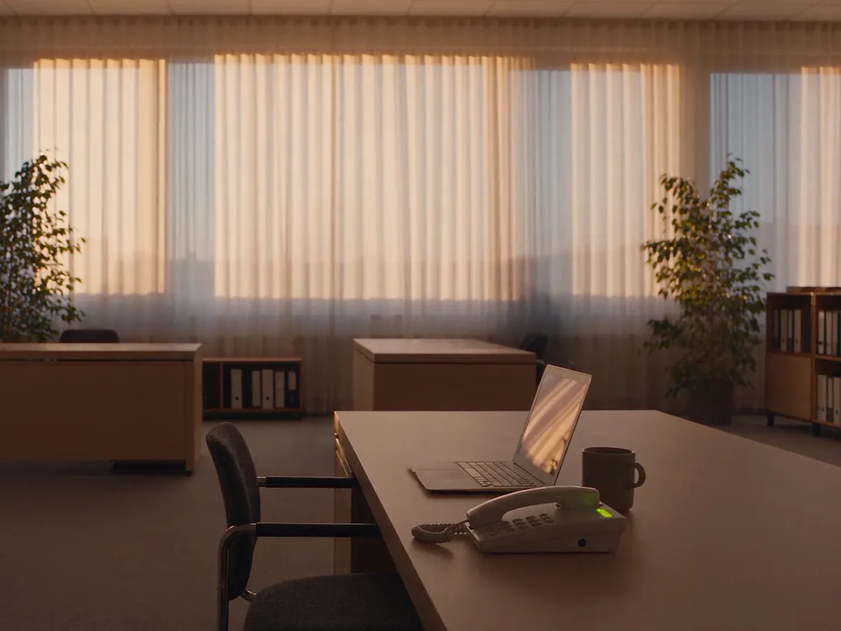 A quiet office in the evening light, with a phone and a laptop on the desk