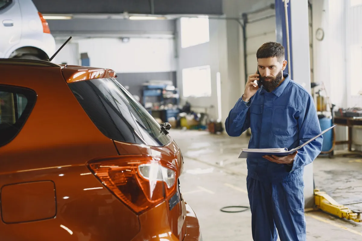 A mechanic takes a phone call in the workshop with a folder in his hand