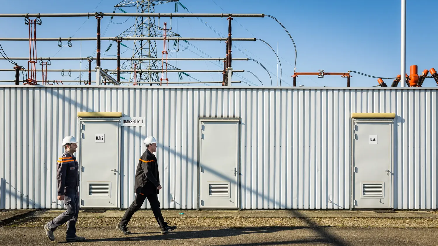 Two engineers with helmets walking past an electricity station