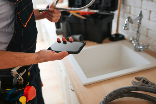 Plumber with tool belt checking a phone by a kitchen tap